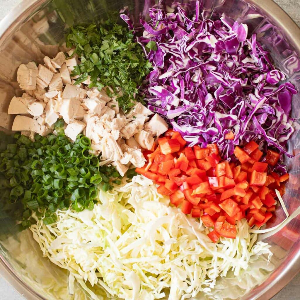 Chopped chicken, cabbage, bell peppers and green onions in a large mixing bowl