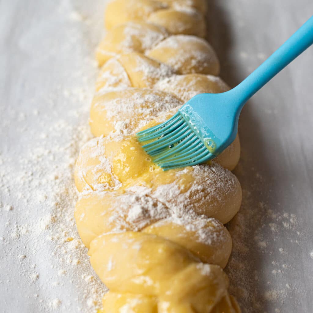 a blue pastry brush putting egg wash onto challah dough before baking