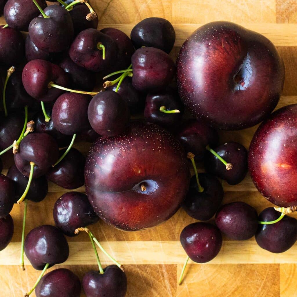 fresh cherries and black plums on a wooden board