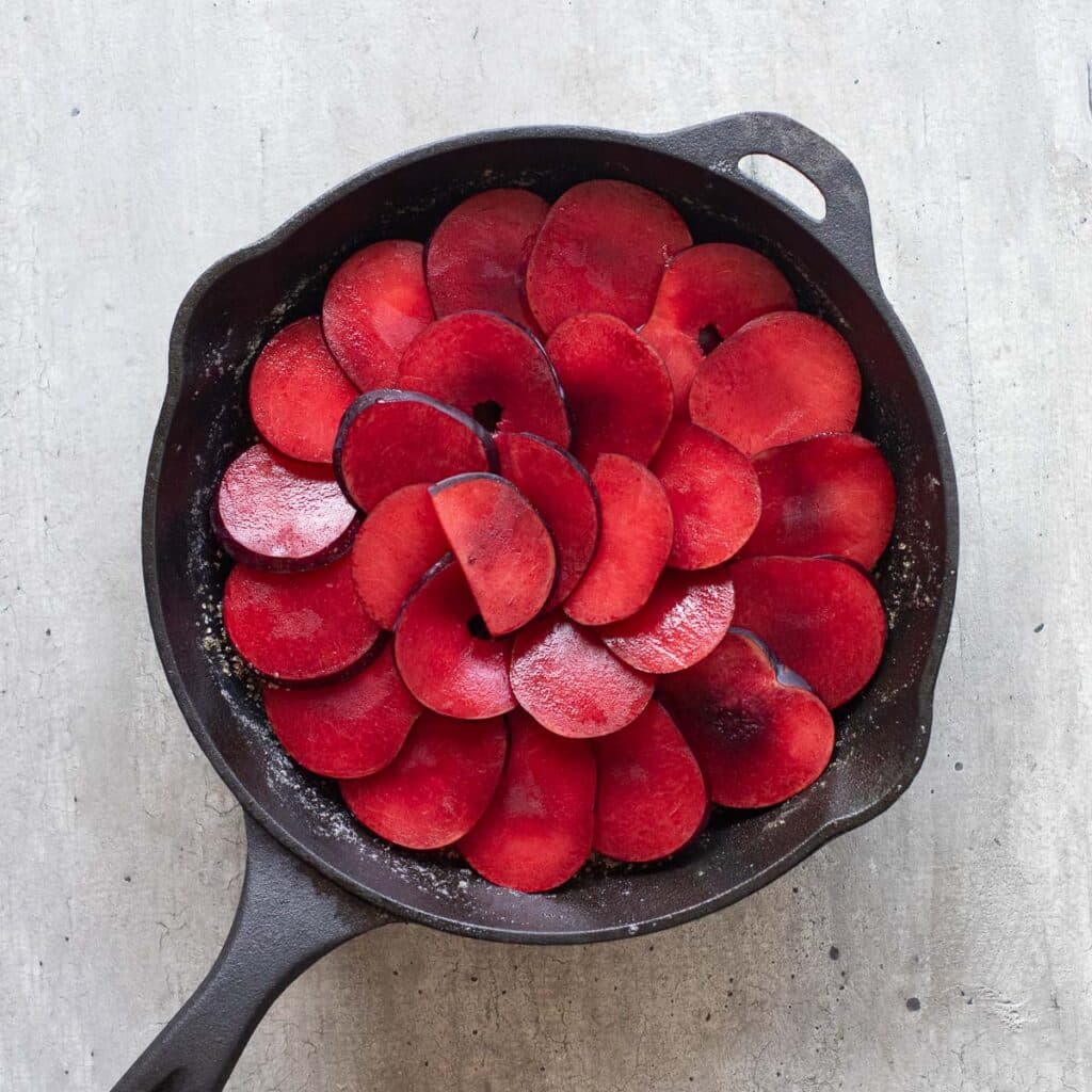 sliced plums layered in an overlapping pattern in a cast iron pan