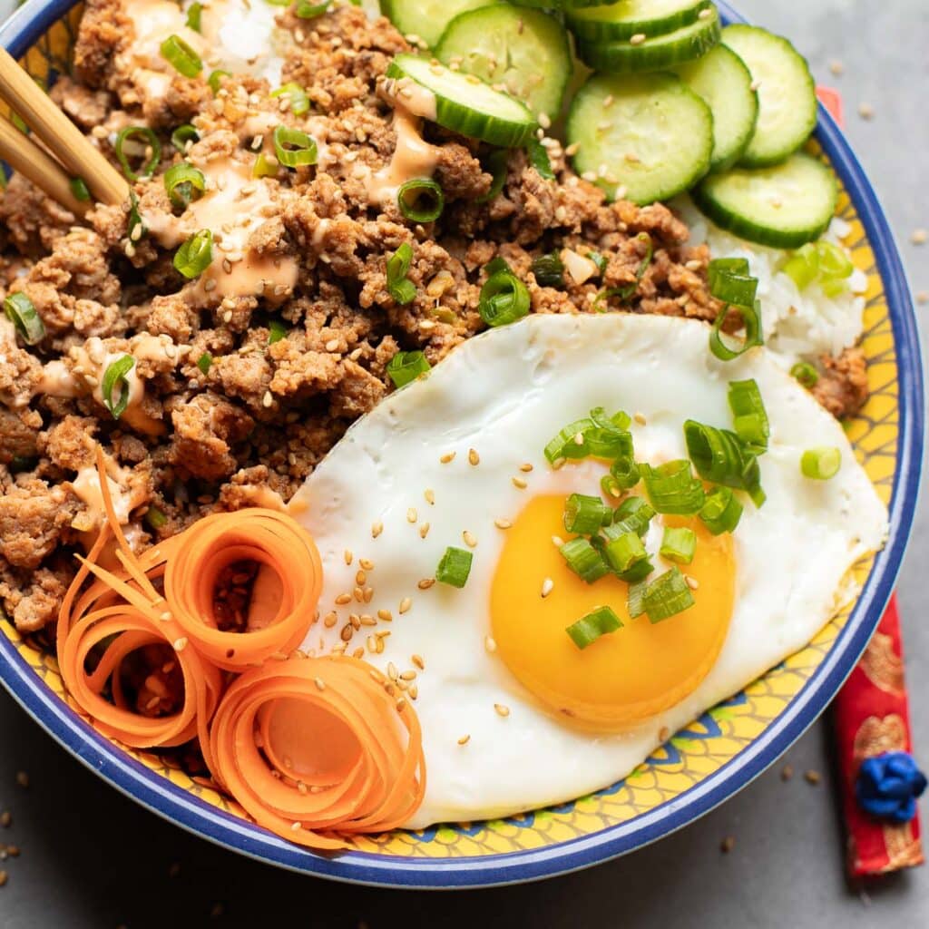 Chicken bibimbap with an egg, sliced cucumbers and grated carrots