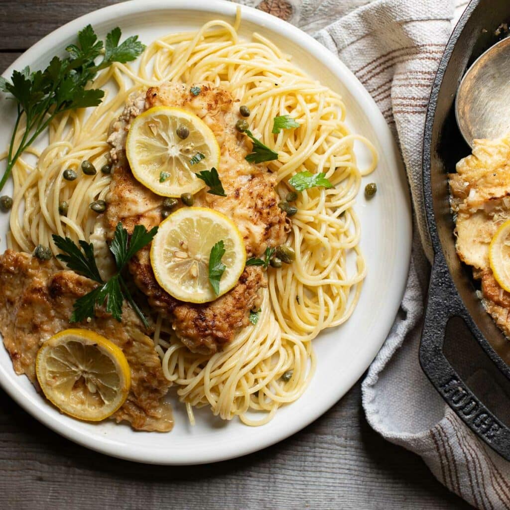 chicken piccata on a bed of pasta on a white plate