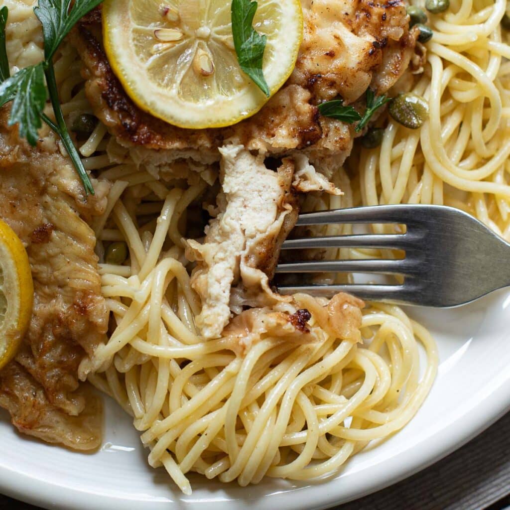 a fork holding a bite of chicken piccata