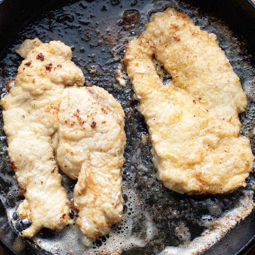 chicken cutlets cooking in a cast iron skillet