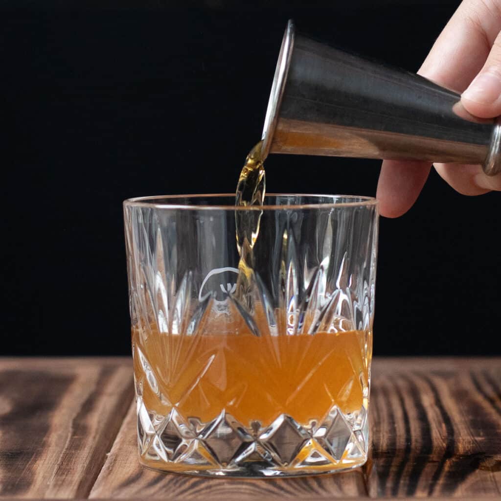 Bourbon being poured into a rocks glass with a silver shot glass
