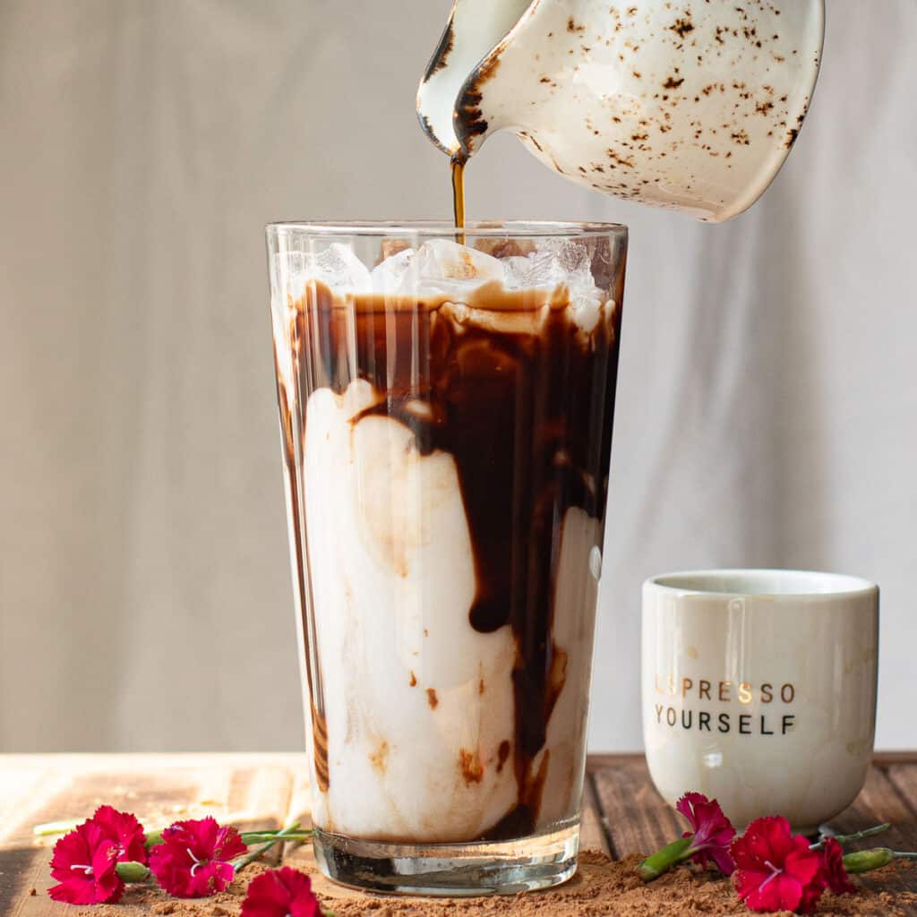 espresso being poured over iced milk in a tall glass