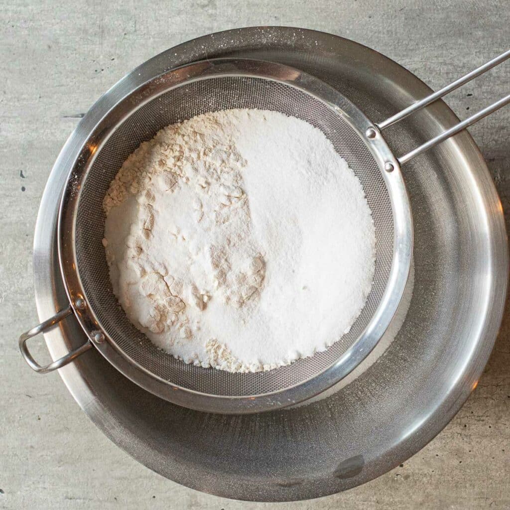 flour and sugar being sifted into a mixing bowl