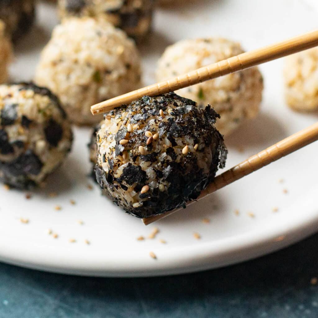 chopsticks holding a Korean rice ball that was rolled in nori flakes