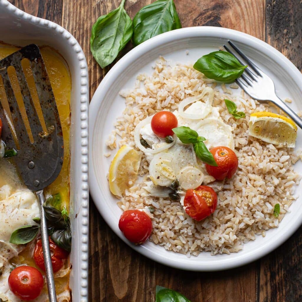 roasted fish on a white plate with brown rice and cherry tomatoes