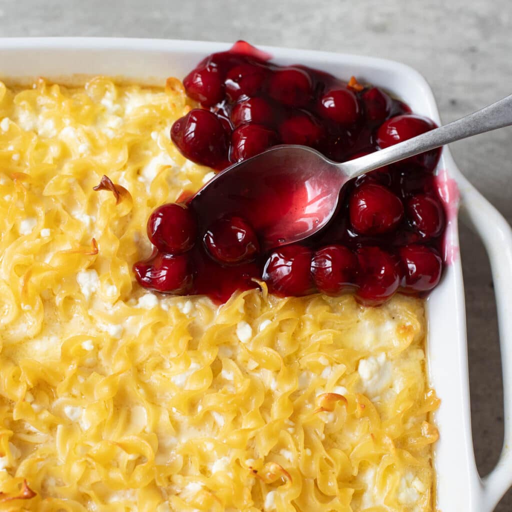 a spoon putting cherries on top of sweet noodle kugel
