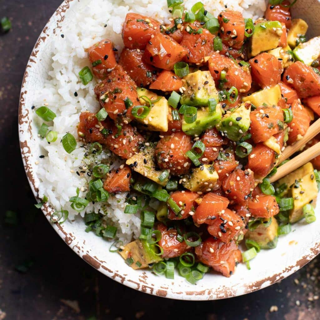 Hawaiian salmon poke over rice in a white bowl with chopsticks