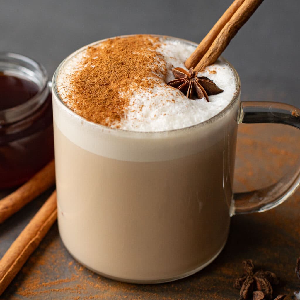 chai latte in a glass coffee mug with a cinnamon stick and star anise