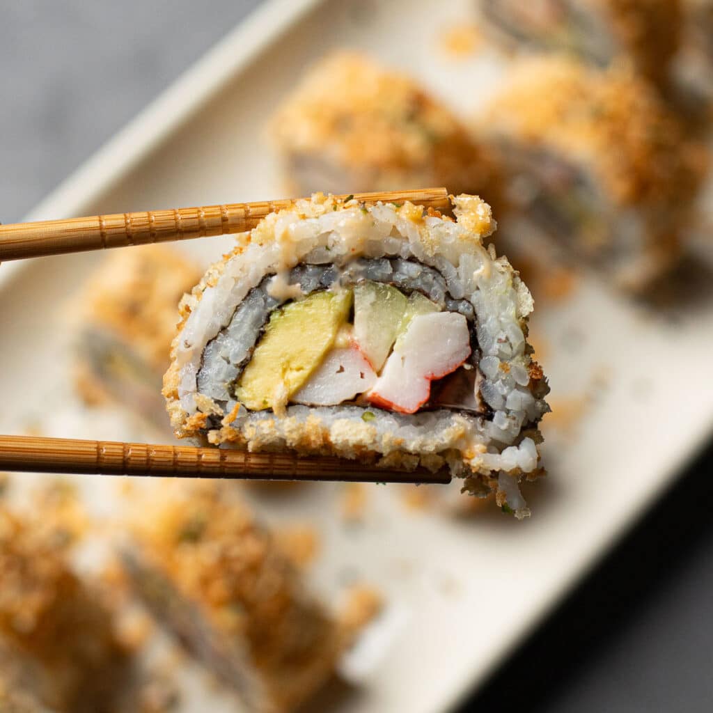 chopsticks holding a piece of crunchy sushi roll
