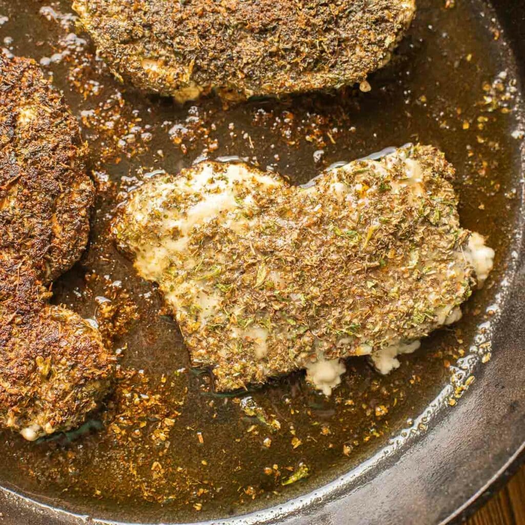 herb crusted chicken cooking in a cast iron skillet