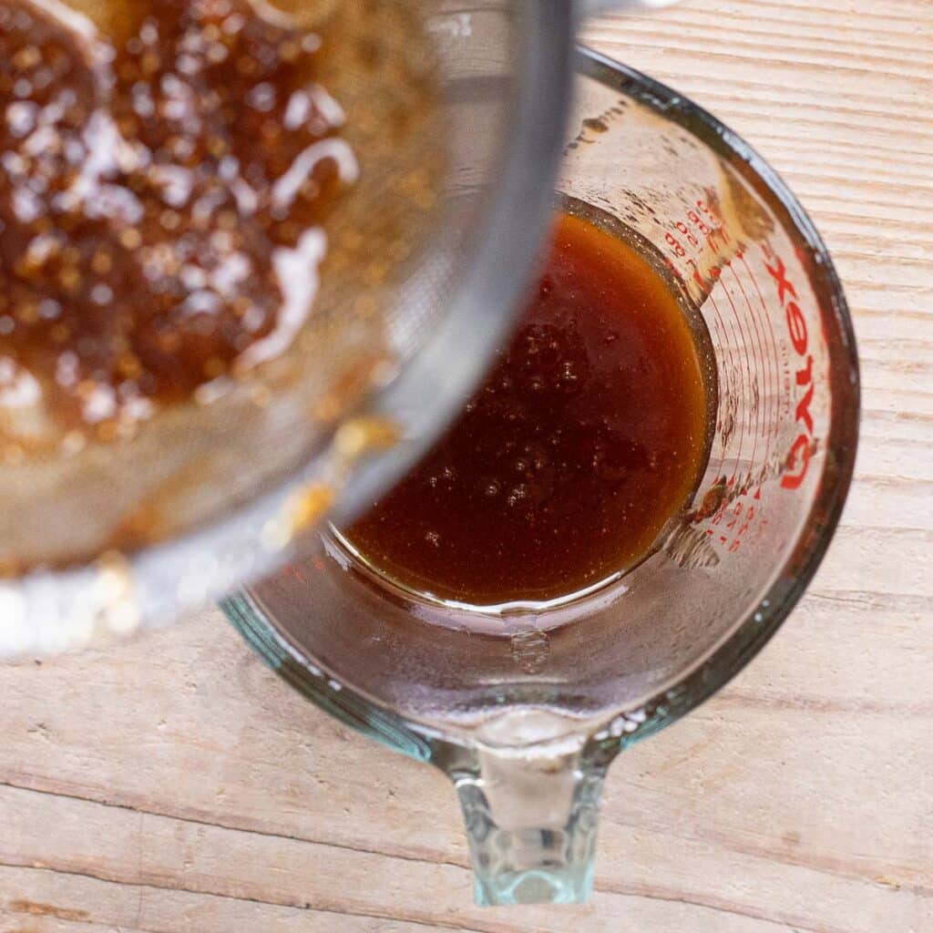 fig syrup being strained into a glass measuring cup