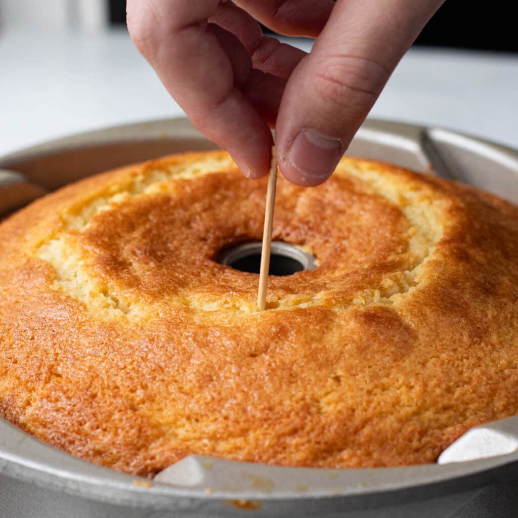 a hand poking holes in the top of a cake with a toothpick