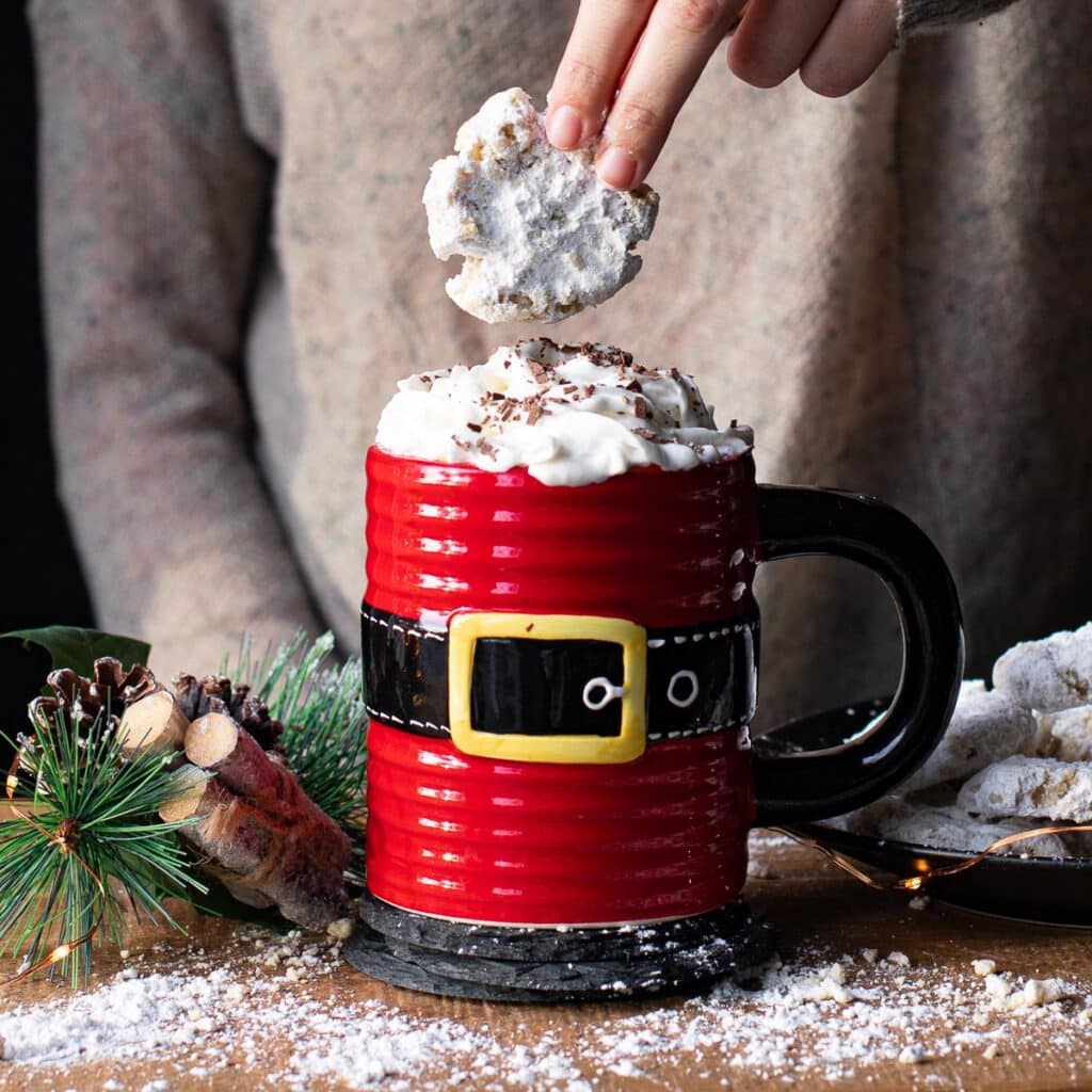 A hand dunking a vanilla almond smash cookie into a santa claus mug