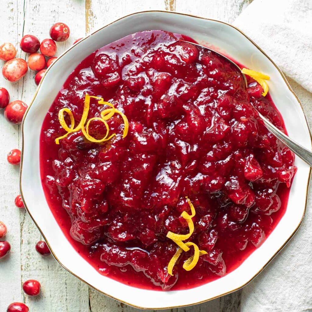 whole cranberry sauce in a white bowl with orange peel as garnish