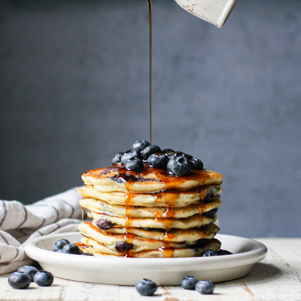 maple syrup pouring on to a stack of blueberry pancakes