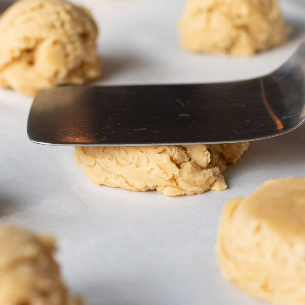 a spatula flattening a ball of cookie dough