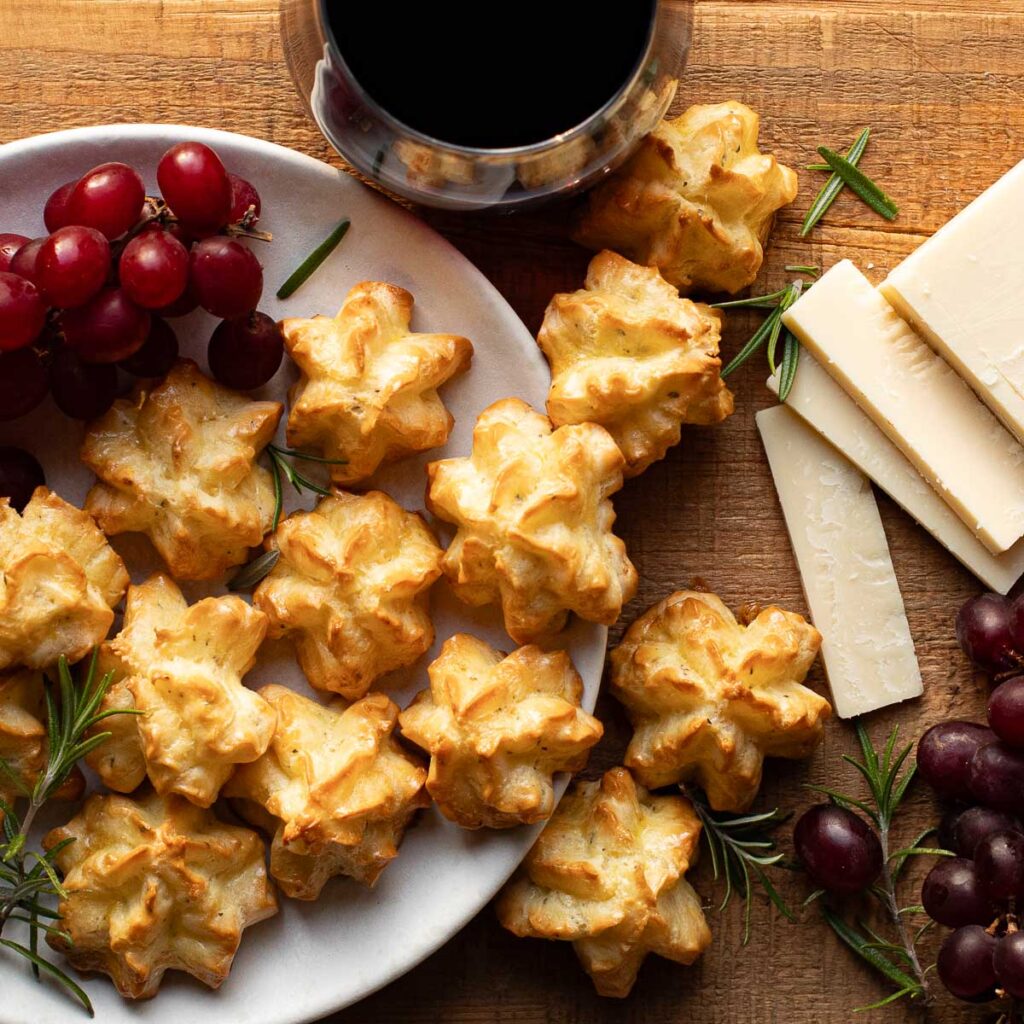 gougeres on a white plate with red grapes and rosemary sprigs