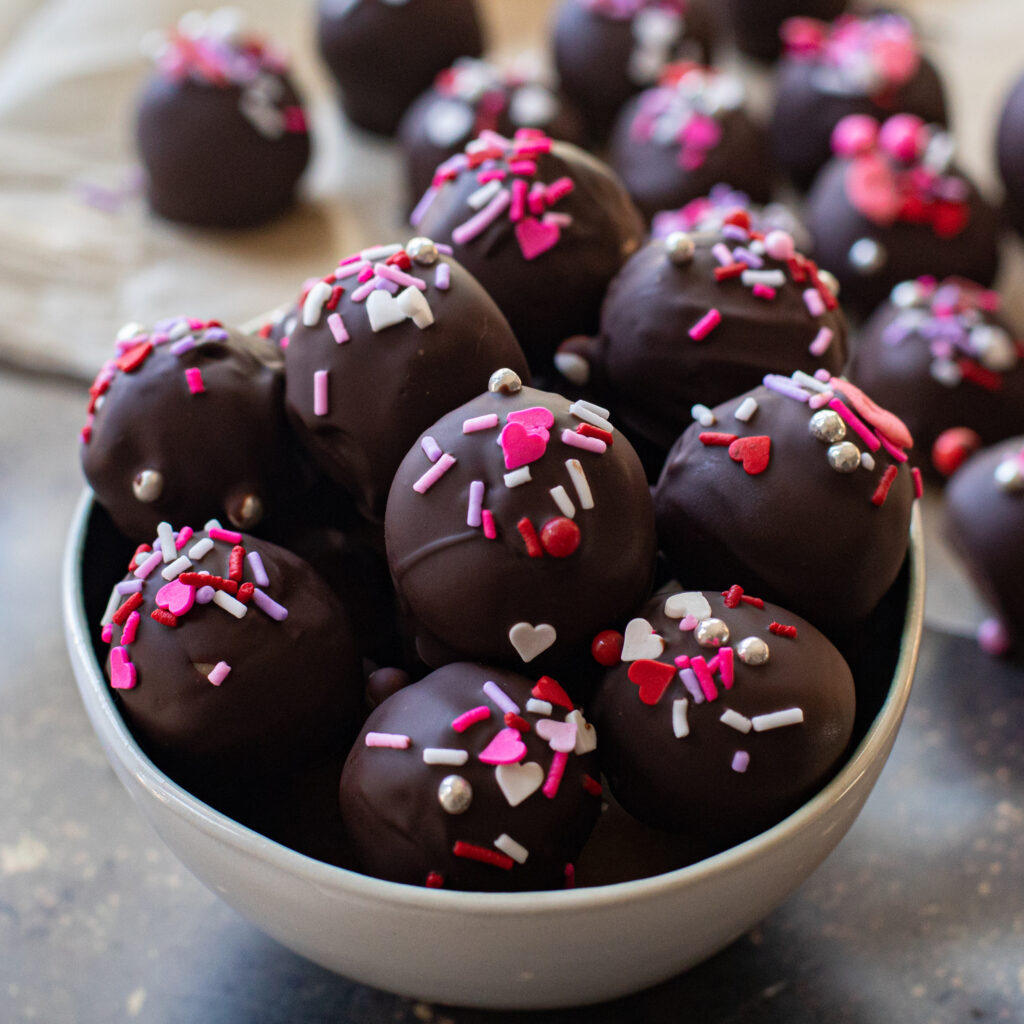 chocolate peanut butter balls in a white bowl decorated with pink and red sprinkles