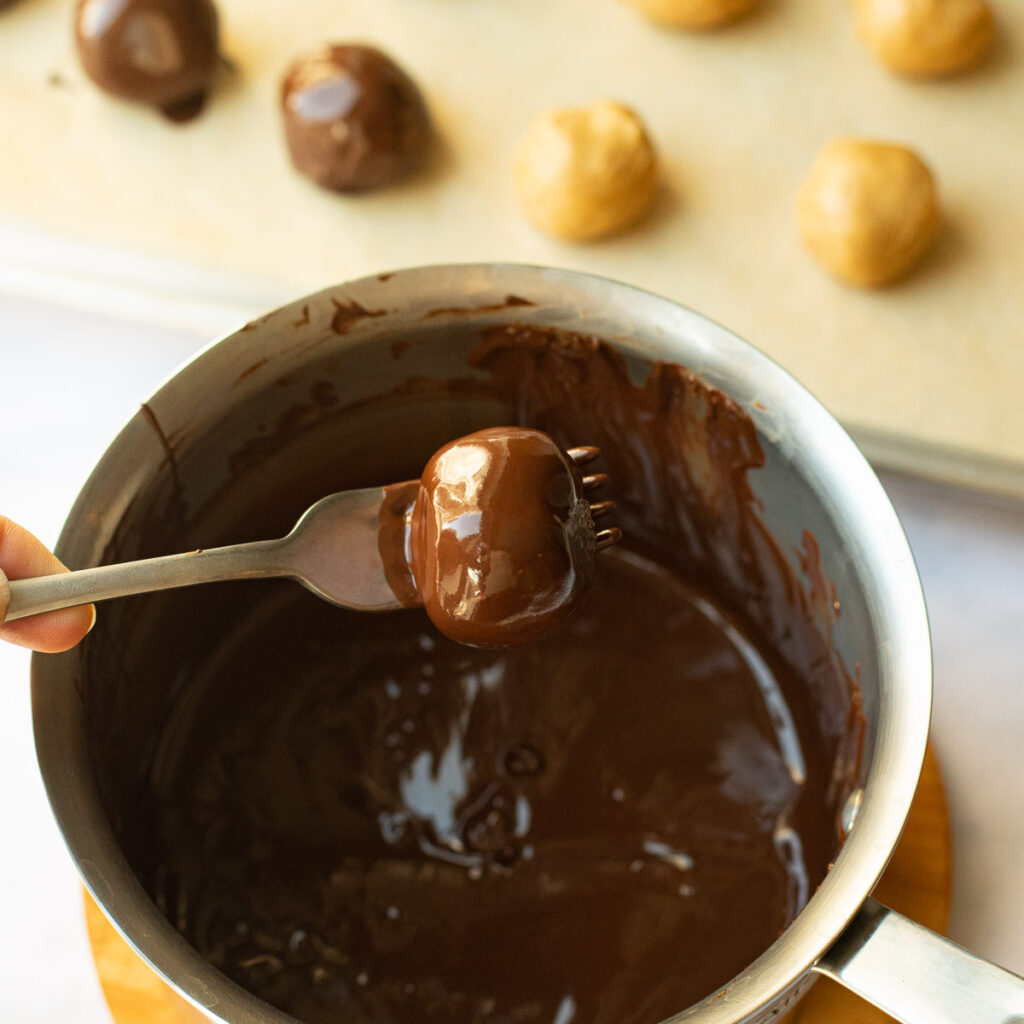 a peanut butter ball being dipped in melted chocolate