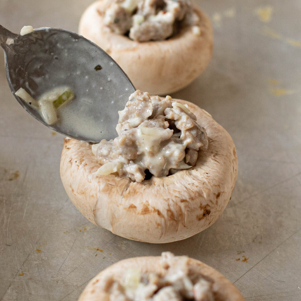 a spoon filling a mushroom cap with sausage stuffing
