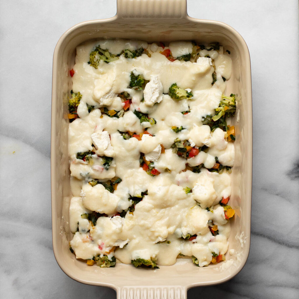 lasagna noodles topped with vegetables and white sauce in a baking dish