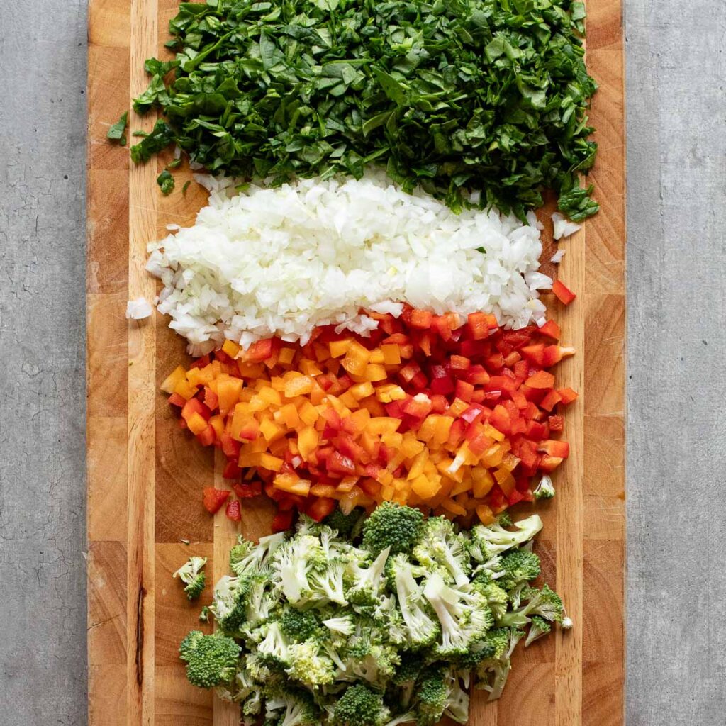 chopped spinach, diced onions, diced bell peppers and chopped broccoli on a wooden board