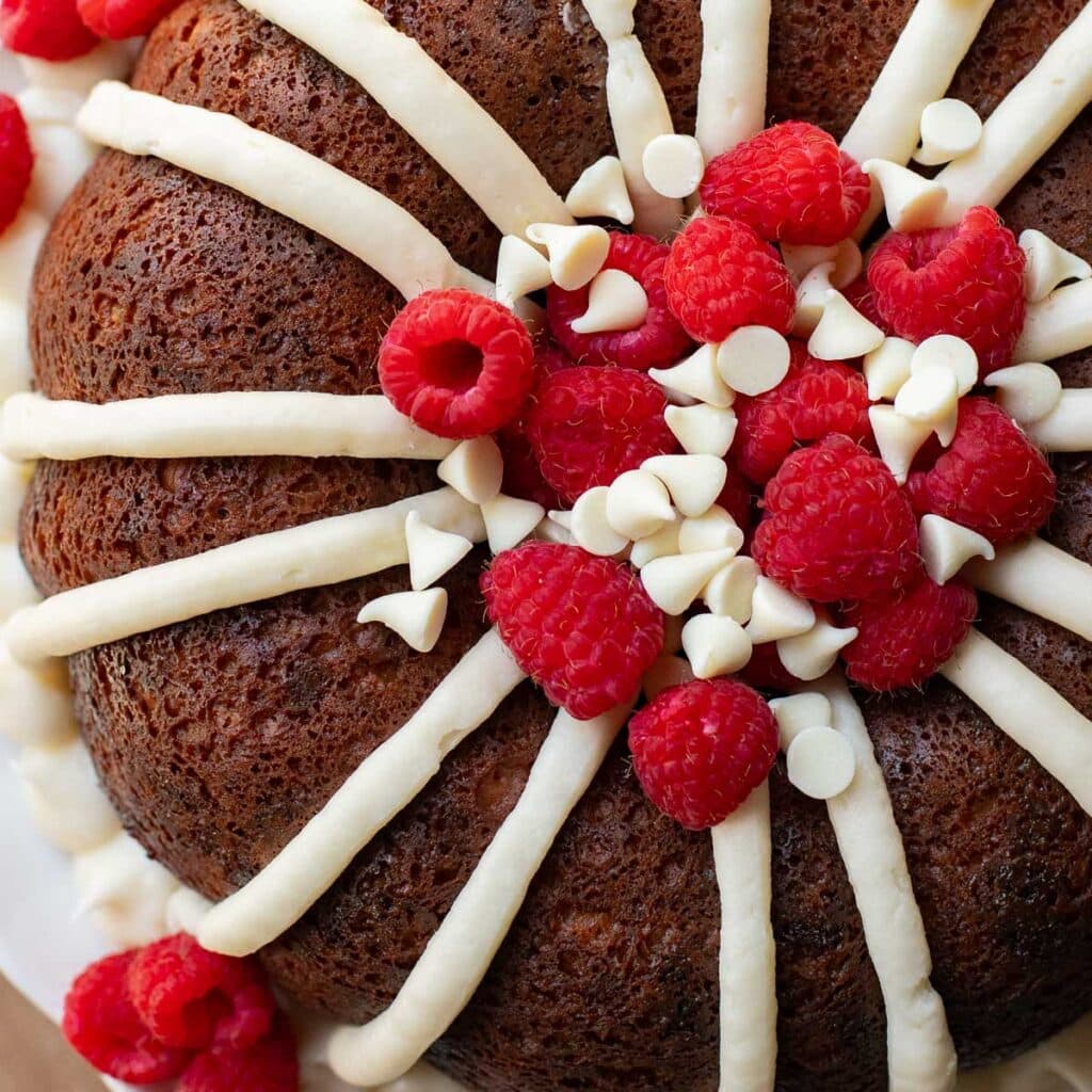 overhead view of nothing bundt cakes white chocolate raspberry cake garnished with cream cheese frosting and fresh raspberries