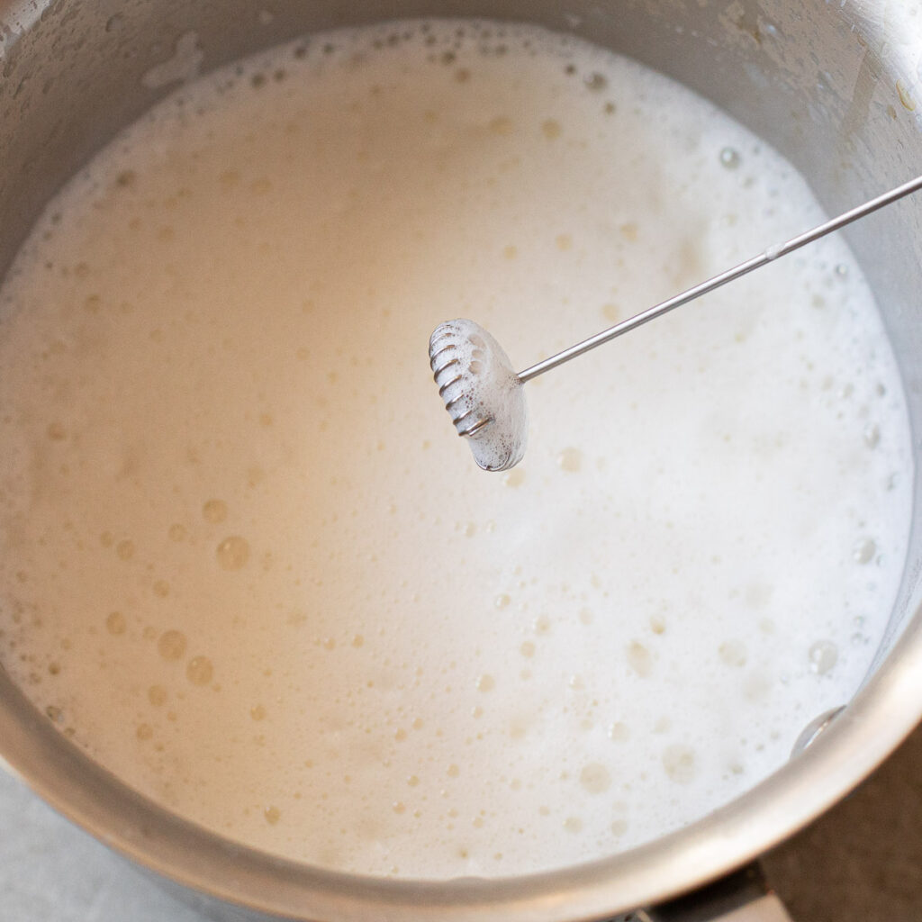 white hot chocolate in a saucepan with a handheld milk frother