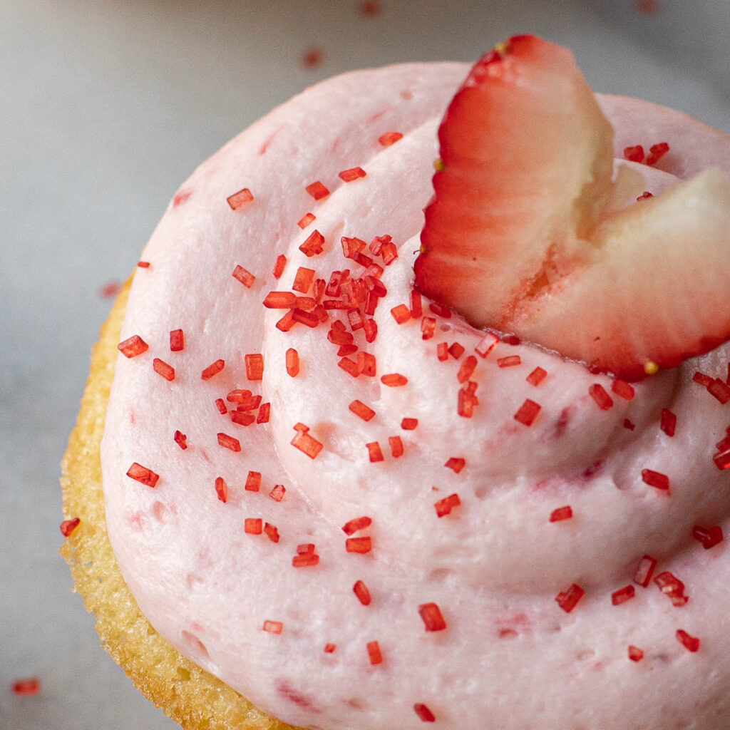strawberry frosting and red sprinkles on top of a Champagne cupcake