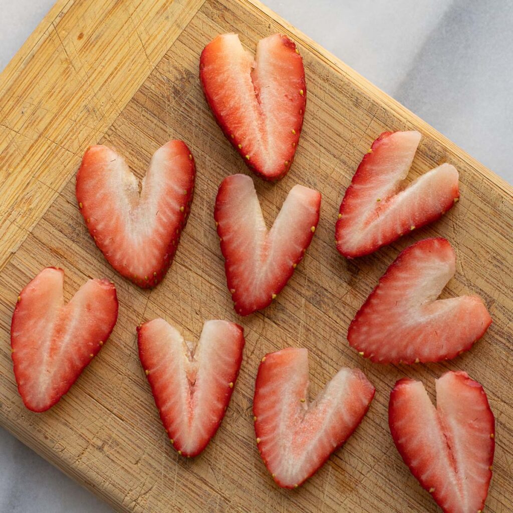 strawberries sliced to look like hearts on a wooden cutting board