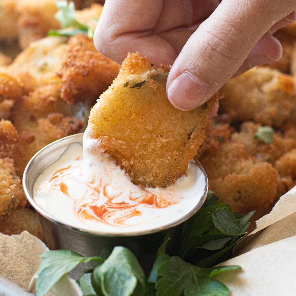 a hand dipping a fried pickle into ranch dressing
