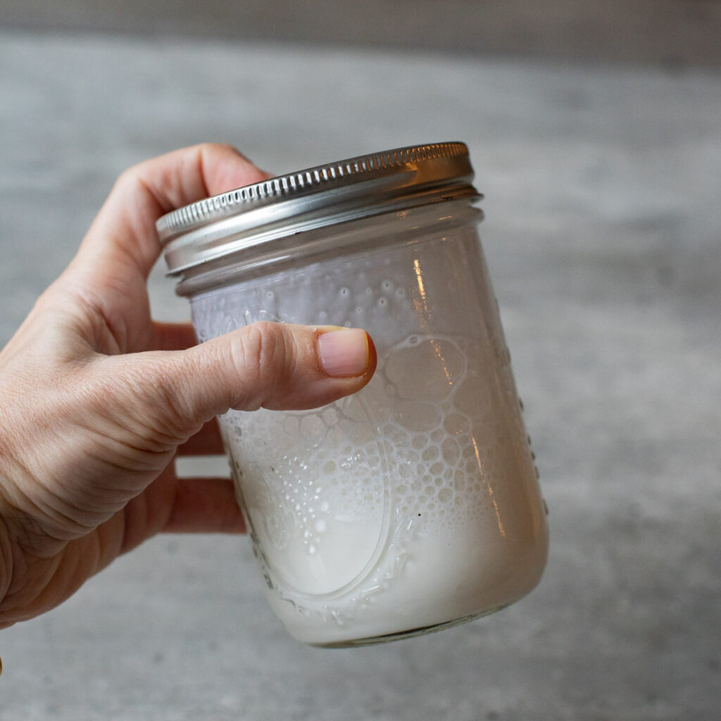 a hand shaking a mason jar filled with milk