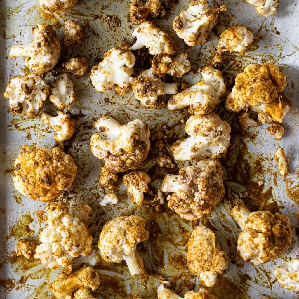 cauliflower florets tossed in Indian spices on a baking sheet