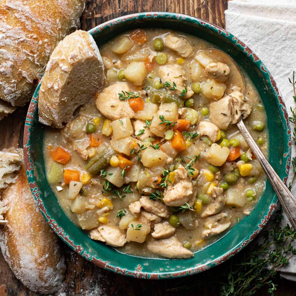 chicken vegetable stew in a green bowl with bread on the side