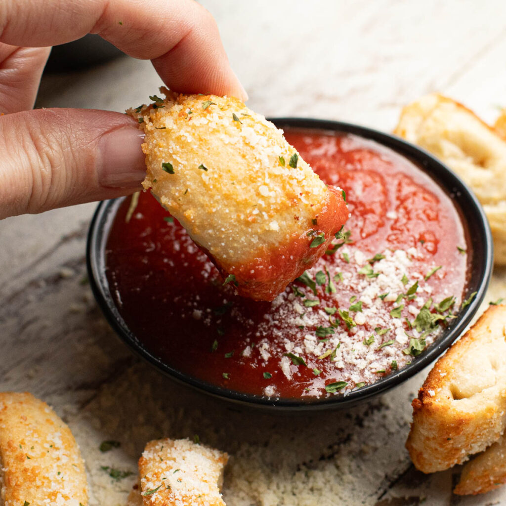 a hand dipping a Dominos Parmesan bite into pizza sauce