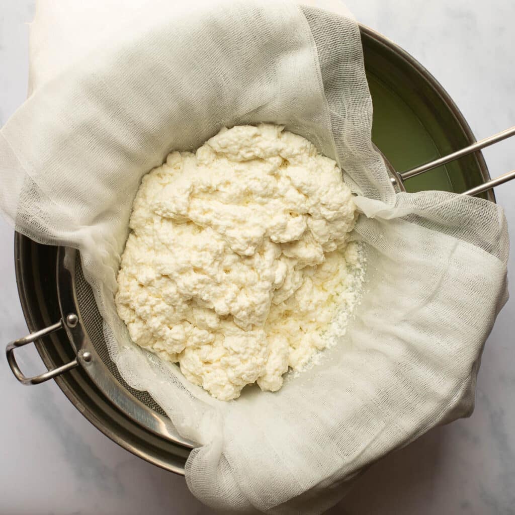 cheese curds sitting in a strainer with a cheesecloth