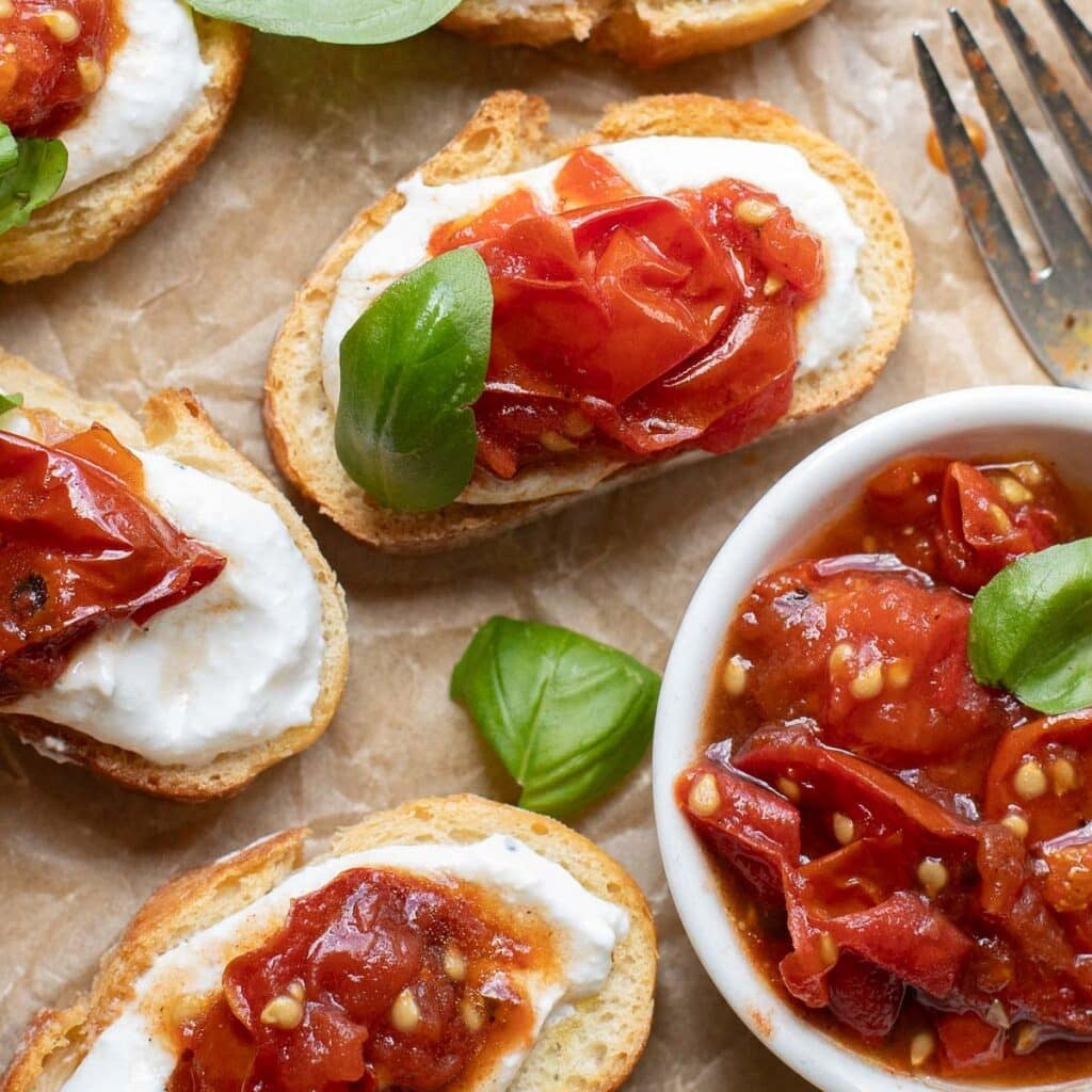 cottage cheese toasts on parchment paper next to a bowl of roasted tomatoes