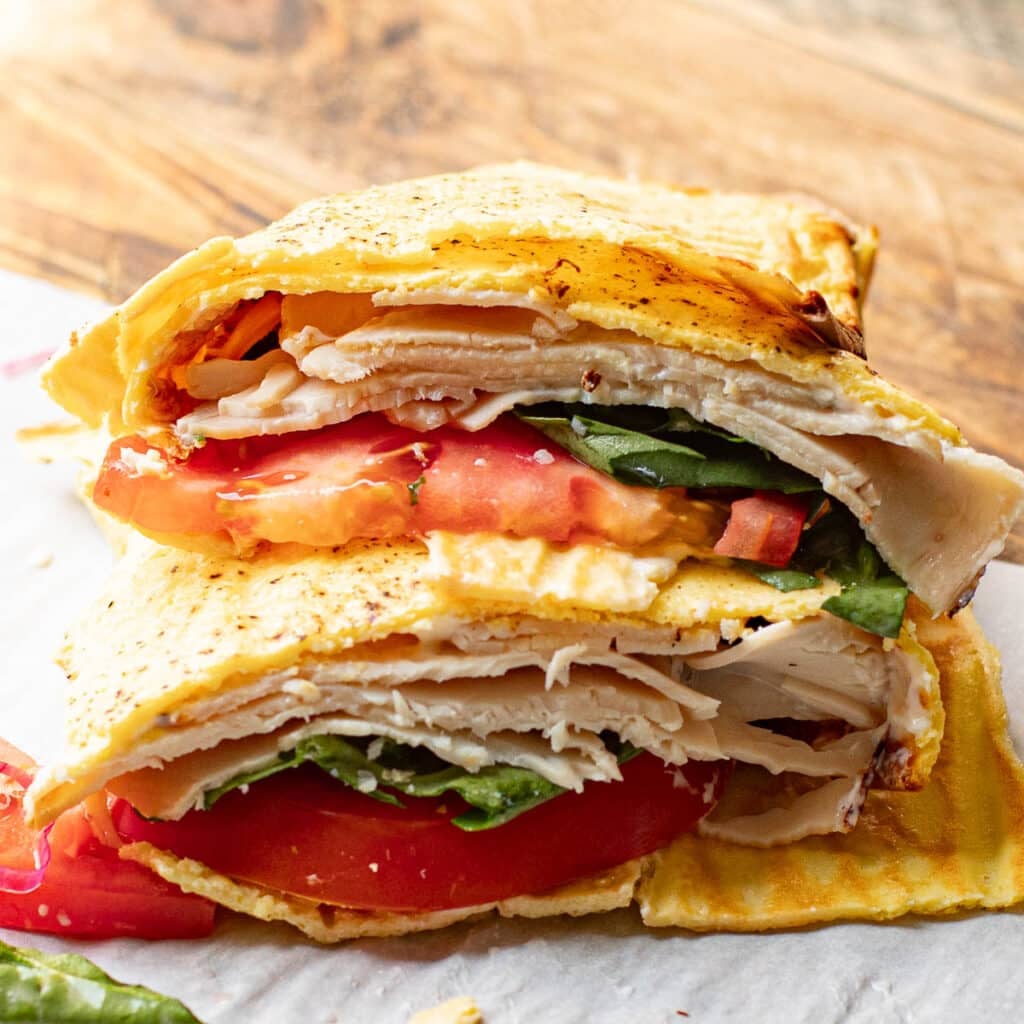 Two halves of a turkey, lettuce and tomato cottage cheese wrap stacked on each other
