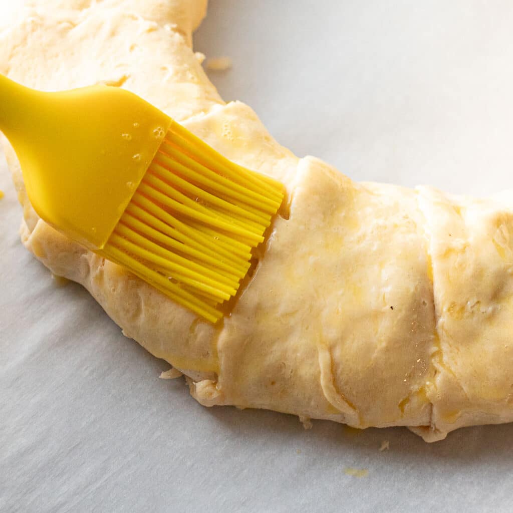 crescent roll wreath being brushed with beaten egg before baking