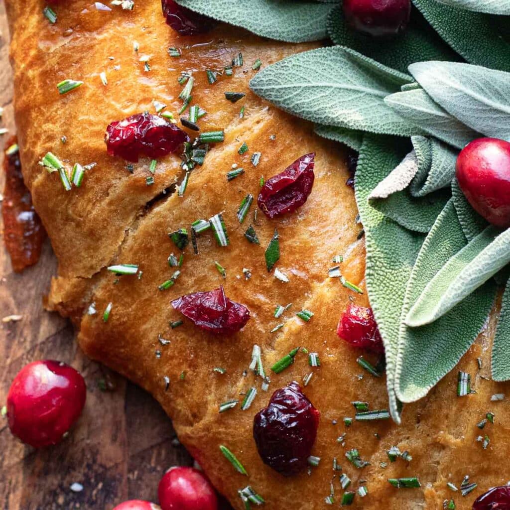 close up of the exterior of brie crescent roll wreath, topped with chopped rosemary and dried cranberries