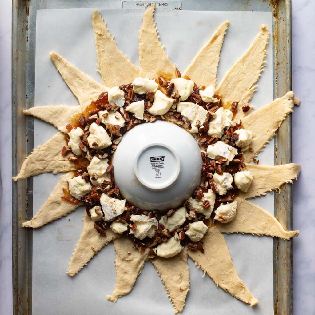 fig jam, brie pieces and chopped pecans layers on top of crescent roll dough that is arranged around a small white bowl