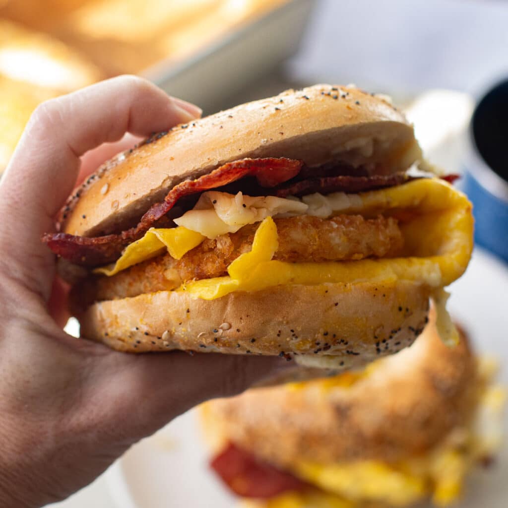 a hand holding a bagel breakfast sandwich