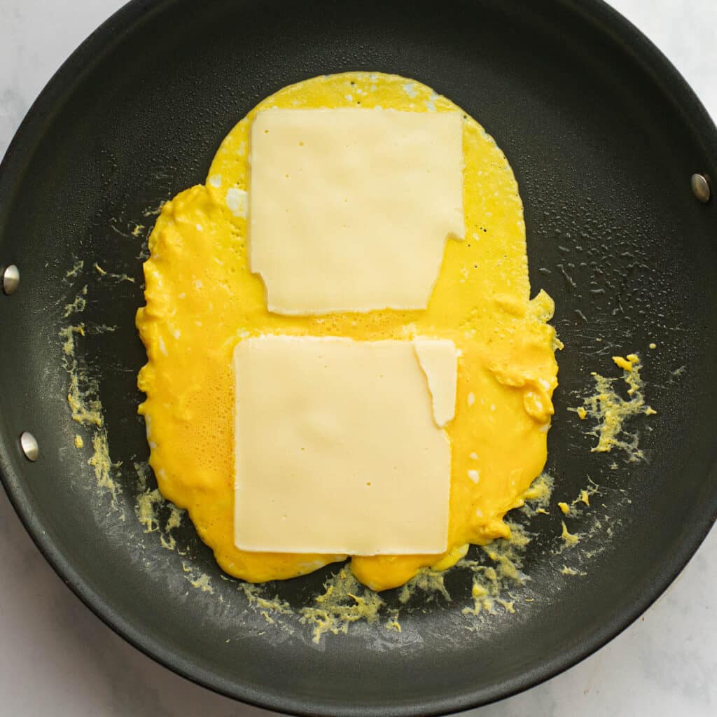 scrambled eggs in a pan with slices of American cheese on top