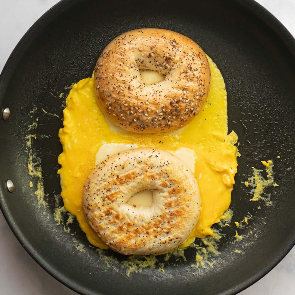 bagel halves on top of scrambled eggs in a pan