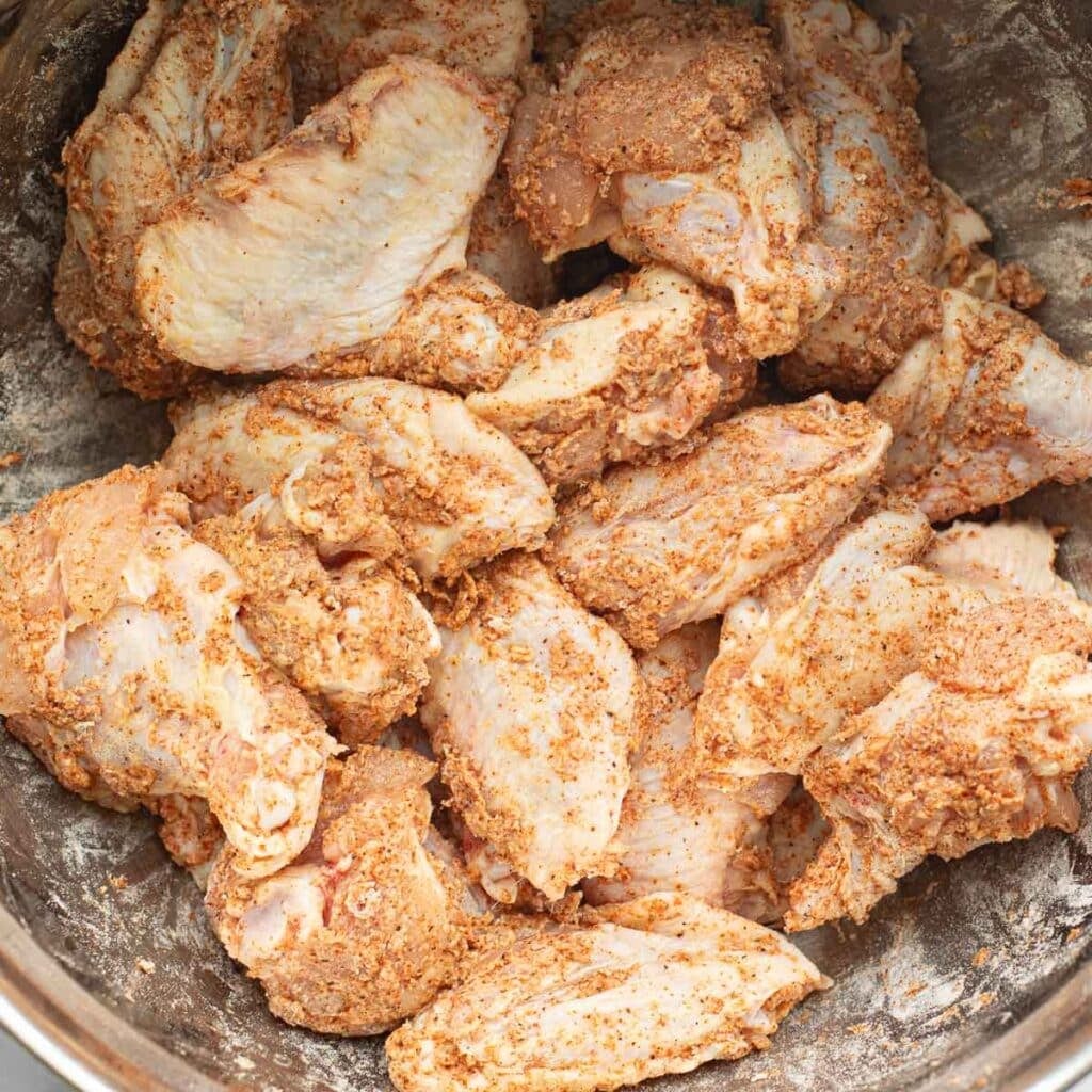 chicken wings tossed in dry seasonings in a mixing bowl