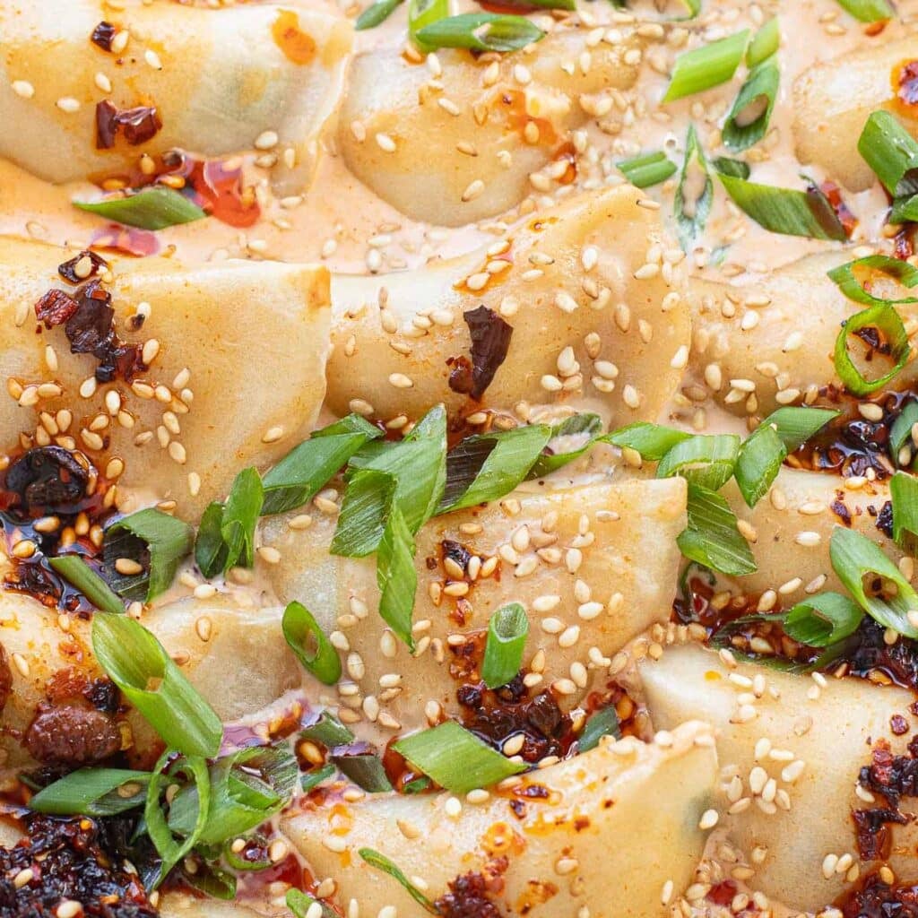 close up of baked dumplings topped with sauce and chopped green onions